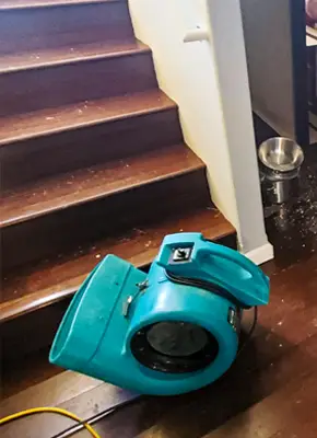 Industrial air blower positioned beside a damp wooden staircase for drying in a Melbourne property
