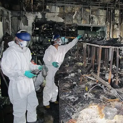 Workers loading burnt materials into a disposal container after a fire