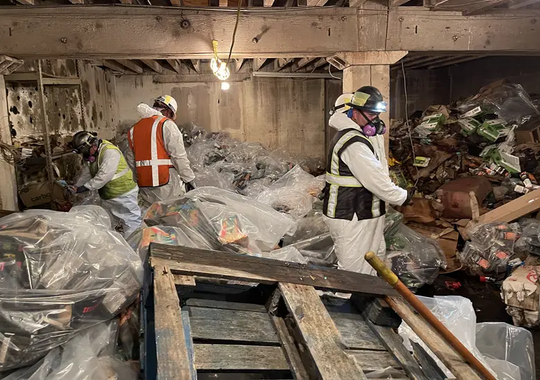 Workers in protective gear sorting and containing fire debris