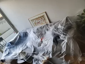 Furniture covered with plastic sheeting to protect it during mould remediation in a Melbourne property.