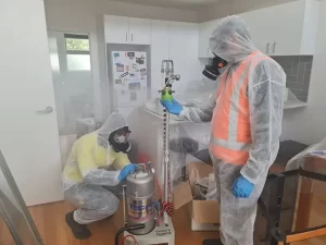 Technicians in hazard uniforms setting up a dry fog disinfection machine in a Melbourne property for sanitization.