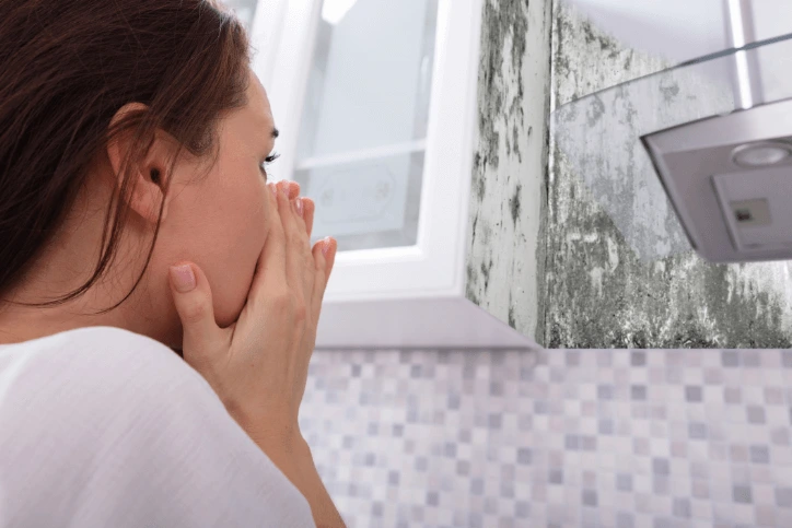 Woman feeling unwell with mould spots on wall behind